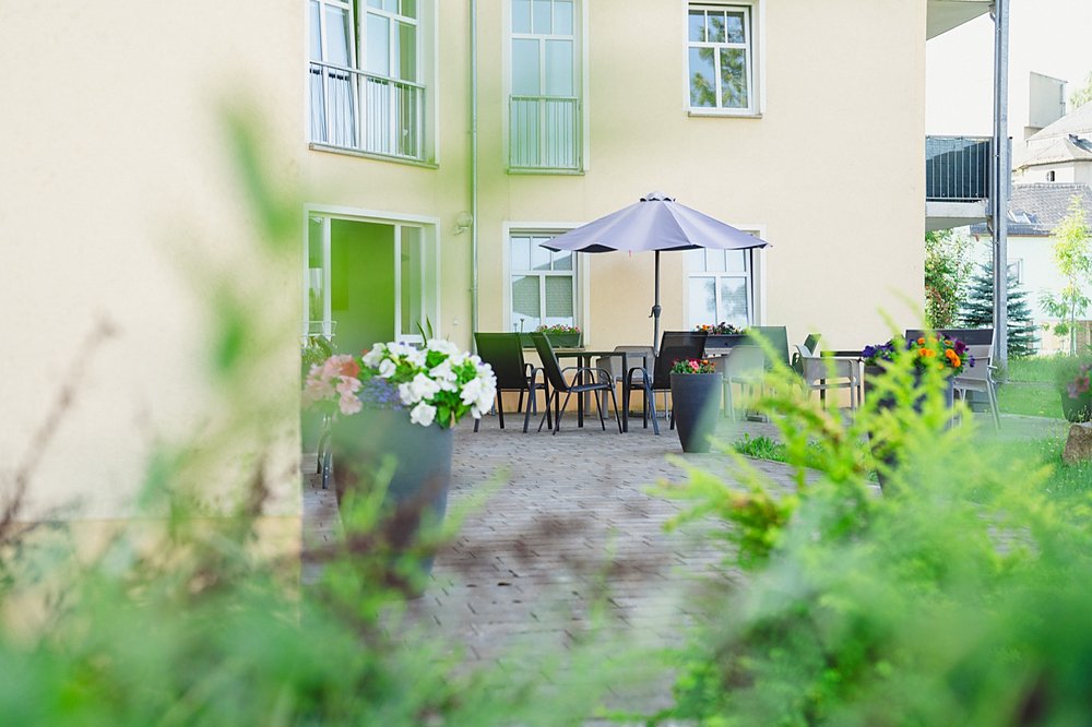 Terrasse im begrünten Innenhof mit Sonnenschirm, Stühlen und blühenden Kübeln