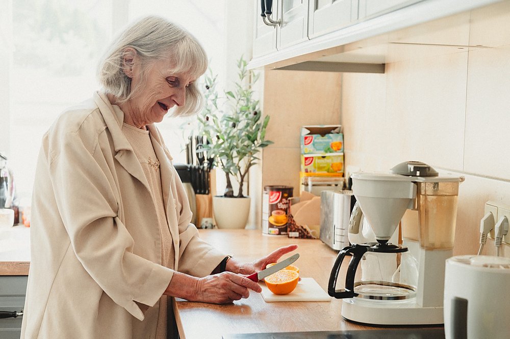 Bewohnerin schneidet an der Küchenzeile eine Orange auf, daneben stehen Kaffeemaschine und Wasserkocher